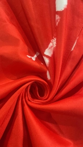 Detailed macro view of spiral folded red fabric with artistic white tie-dye print patterns