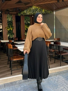 Détail d'un pull en maille marron avec une jupe plissée noire et une ceinture large