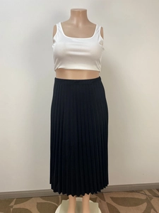 Détail du haut court blanc à col en U et de la jupe mi-longue plissée noire sur mannequin