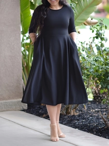 Detail view of slim fit black midi dress with round neck and high waist pleated skirt