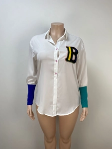 Detail of white oversized shirt featuring multi-color B patch and asymmetrical cuffs
