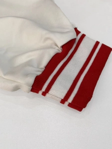 Detail of white long sleeve jacket featuring red elastic ribbed cuffs with white stripes