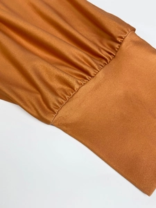 Detail of deep orange satin dress fabric showing glossy silk texture and pleated cuff edges