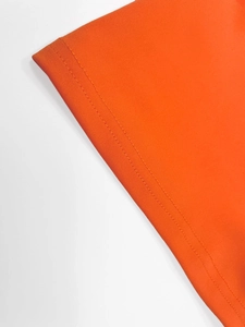 Detailed close-up of bright orange knit fabric with precise double-needle stitching on hem