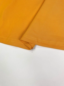 Detailed close-up of double-needle stitching on the hem of a vibrant orange knit dress