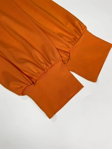Close-up of elastic cuffs and pleated texture on an orange-red knit V-neck maxi dress