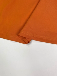 Detail of the orange V-neck dress showing fine jersey texture and neat double-needle hem