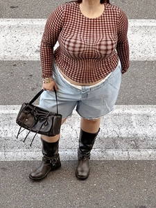 Dettaglio di un top a rete scozzese rosso-marrone con shorts in denim e stivali neri
