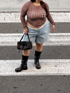 Dettaglio top a rete a quadri marroni con pantaloncini di denim e stivali neri in pelle
