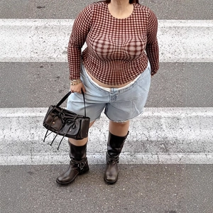 Top a rete a quadri marrone-rosso con pantaloncini di jeans e stivali da motociclista