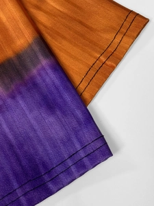Macro shot of orange and purple gradient knit fabric with vertical stripes and stitched hem