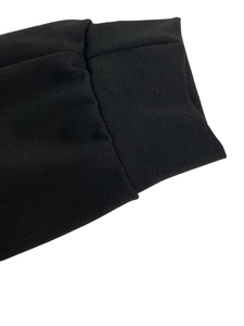 Détail macro du poignet en maille noire avec texture côtelée et coutures minimalistes