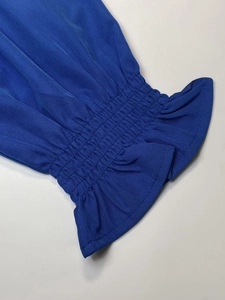 Detail of smocked elastic cuffs with ruffled edges on a blue V-neck long sleeve top
