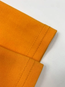 Detail view of the orange knit dress showing high-quality double-needle stitching on cuffs