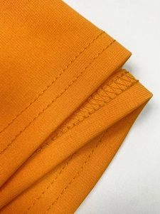 Detail of orange knit dress showing double-needle stitching and overlock seam quality