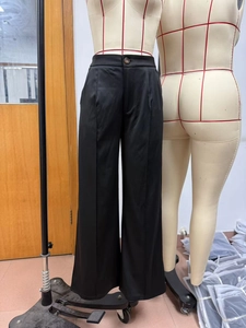 Macro detail of high-waist black wide-leg trousers featuring front pleats on a mannequin