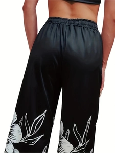 Detail view of black satin wide-leg pants featuring white floral print and elastic waist