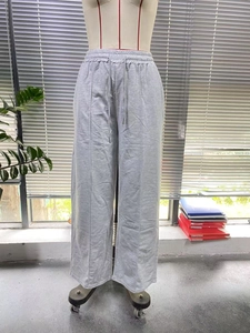 Detail of light grey wide-leg trousers showing drawstring waist and front pleat texture