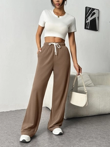 Detail view of brown wide-leg knit trousers with elastic drawstring waist and white crop top