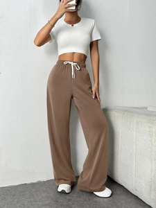 Detail view of brown wide-leg sweatpants featuring elastic waist and white drawstring design