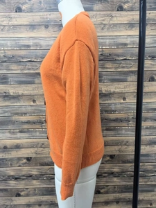 Detail view of orange knit cardigan showing ribbed cuffs and dark button fastening