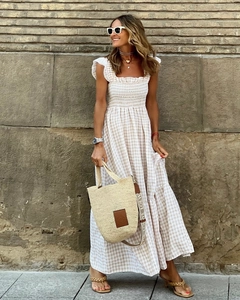 Detail of checkered tiered dress with ruffles and a straw tote bag in a sunny outdoor setting