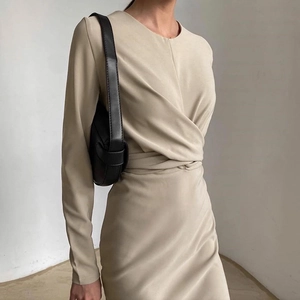 Dettaglio di un abito beige a maniche lunghe con vita aderente e design a pieghe morbide