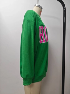 Détail d'un sweat vert côtelé avec la lettre H rose brodée sur la poitrine