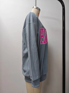 Détail d'un sweat-shirt bleu clair en velours côtelé avec lettrage HO rose et texture