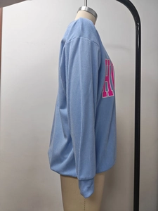 Détail du sweat bleu clair côtelé montrant la texture douce et l'imprimé lettre rose