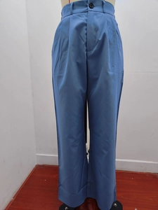 Detail of high-waist blue trousers featuring single button closure and sharp front pleats