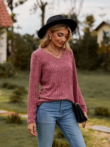 Detalle de blusa de punto acanalado rosa con cuello en V, collar y bolso de cadena