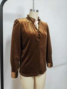 Détail macro du tissu en velours bronze montrant des plis élégants et des boutons sur le chemisier