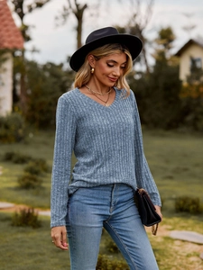 Detalle de top azul de punto con cuello en V, vaqueros y bolso de hombro negro
