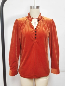 Détail du col en V à volants et boutons noirs sur chemise en velours orange brillant