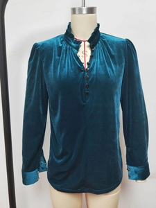 Détail d'une chemise en velours bleu paon avec col à volants et boutons dorés aux poignets