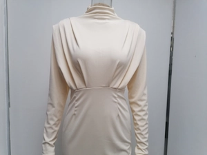 Detail van beige jurk met lange mouwen, voorzien van een coltrui en geplooide schouders