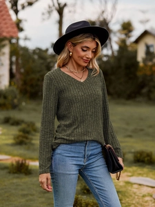Detalle de blusa de punto acanalado verde oliva con cuello en V, joyas y bolso de cadena