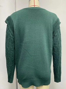 Detail of dark green chunky knit sweater featuring cable knit sleeves and shoulder ruffles