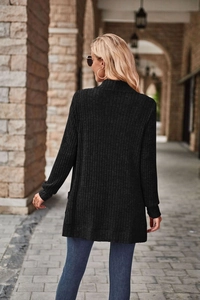Outdoor back view of a woman wearing a black ribbed knit long cardigan in a classic archway
