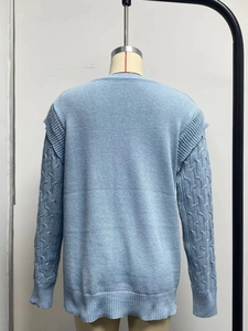 Detail of light blue knit sweater featuring cable knit sleeves and ruffled shoulder design