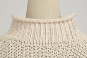 Primer plano de jersey de punto crema con cuello alto acanalado y textura de nido