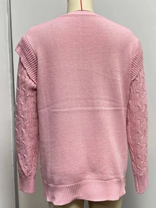 Close-up of pink cable knit sweater featuring ruffled shoulder and ribbed sleeve details