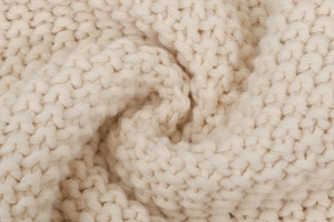 Primer plano de tejido de punto grueso en color crema con textura de lana suave y puntos en V