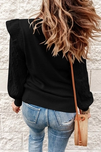 Detail of cable knit sleeves and ruffle shoulder design on a black knitted sweater