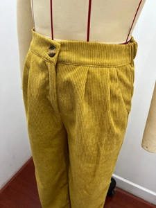 Detailed view of high-waisted mustard yellow corduroy pants with ribbed texture and single button
