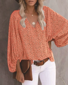 Detail des V-Ausschnitts und weißen Blumendrucks auf der leuchtend orangefarbenen Bluse