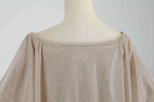 Detail of champagne gold sequined fabric with off-shoulder ruffle neckline and metallic texture