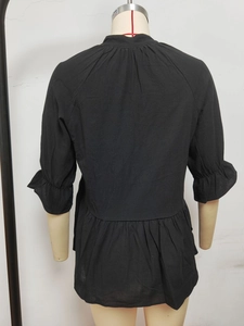 Detail view of the pleated hem and ruffle cuffs on the back of a black V-neck blouse