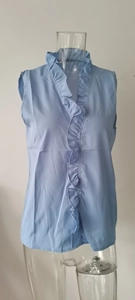 Dettaglio della camicetta senza maniche in chiffon azzurro con scollo a V e balze decorative